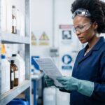 An HSE professional in chemical-handling PPE reviewing a safety data sheet in an industrial storage setting, representing AOAL's article on South Africa's Hazardous Chemical Agents Regulations